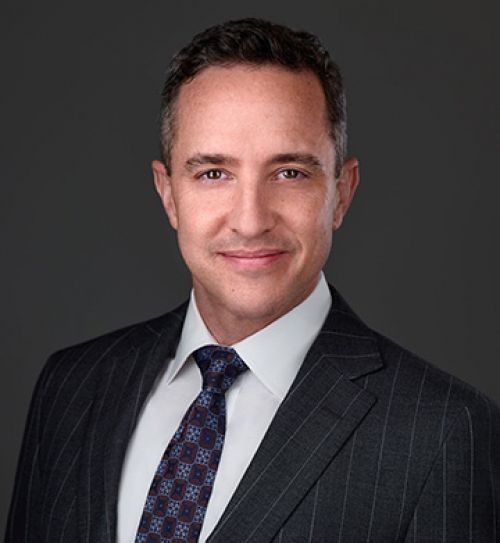 Attorney Matt Horak in a suit smiling against a gray background for a profile or business headshot photo.