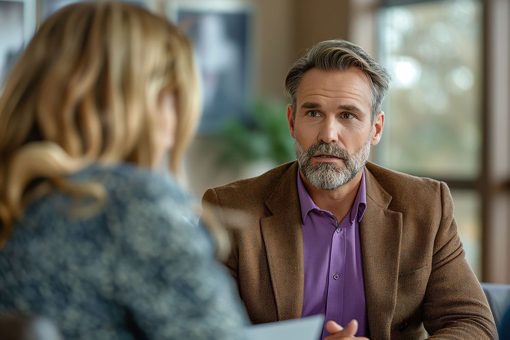 Professional man in a brown blazer having a conversation with a woman in an office setting.