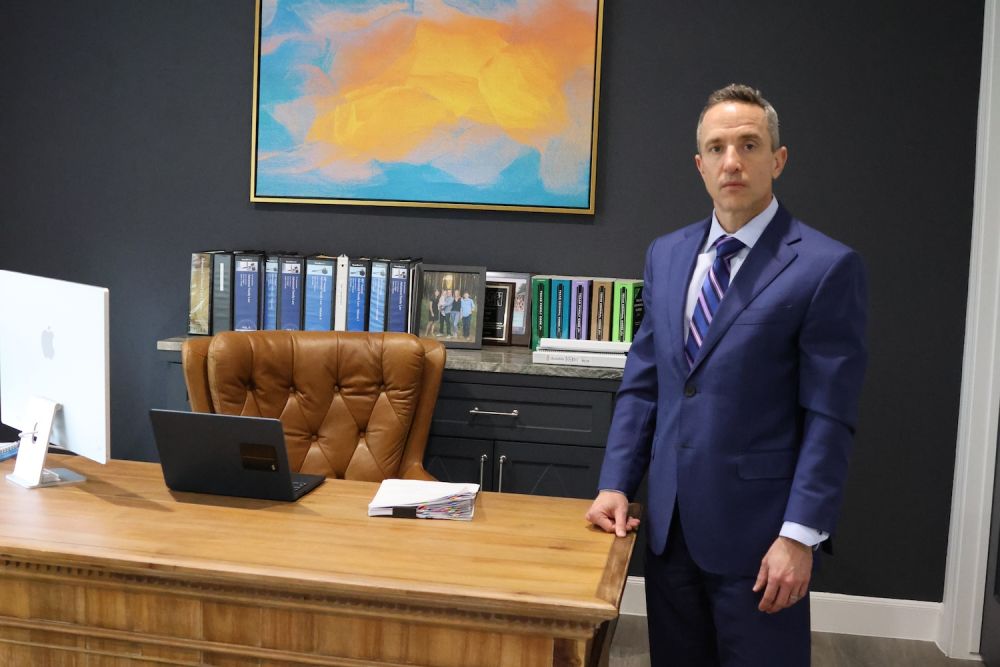 Matthew P. Horak in suit standing by a wooden desk in modern office with colorful abstract art on dark wall.