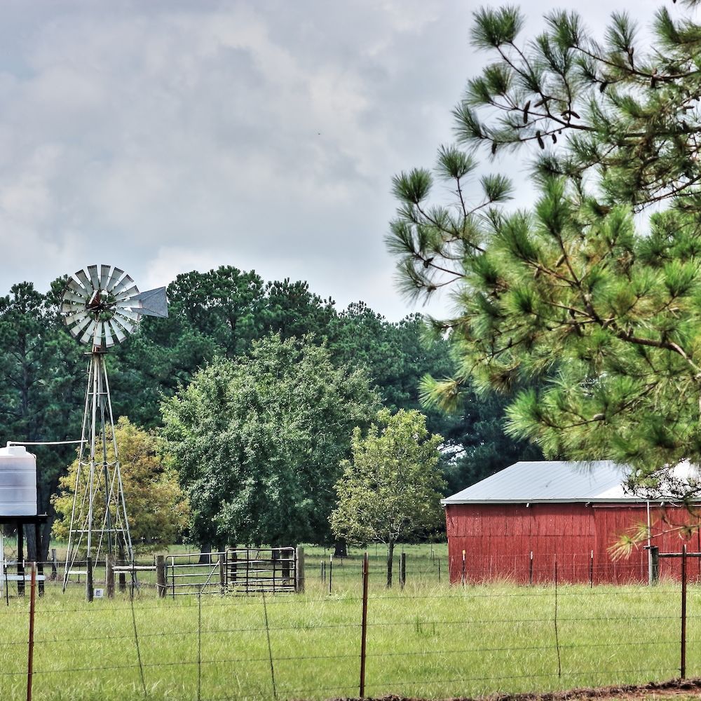 Scenic rural landscape with a windmill, red barn, trees, and spacious green field.