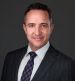 Attorney Matt Horak in a suit smiling against a gray background for a profile or business headshot photo.