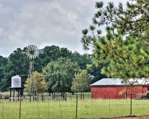Scenic rural landscape with a windmill, red barn, trees, and spacious green field.