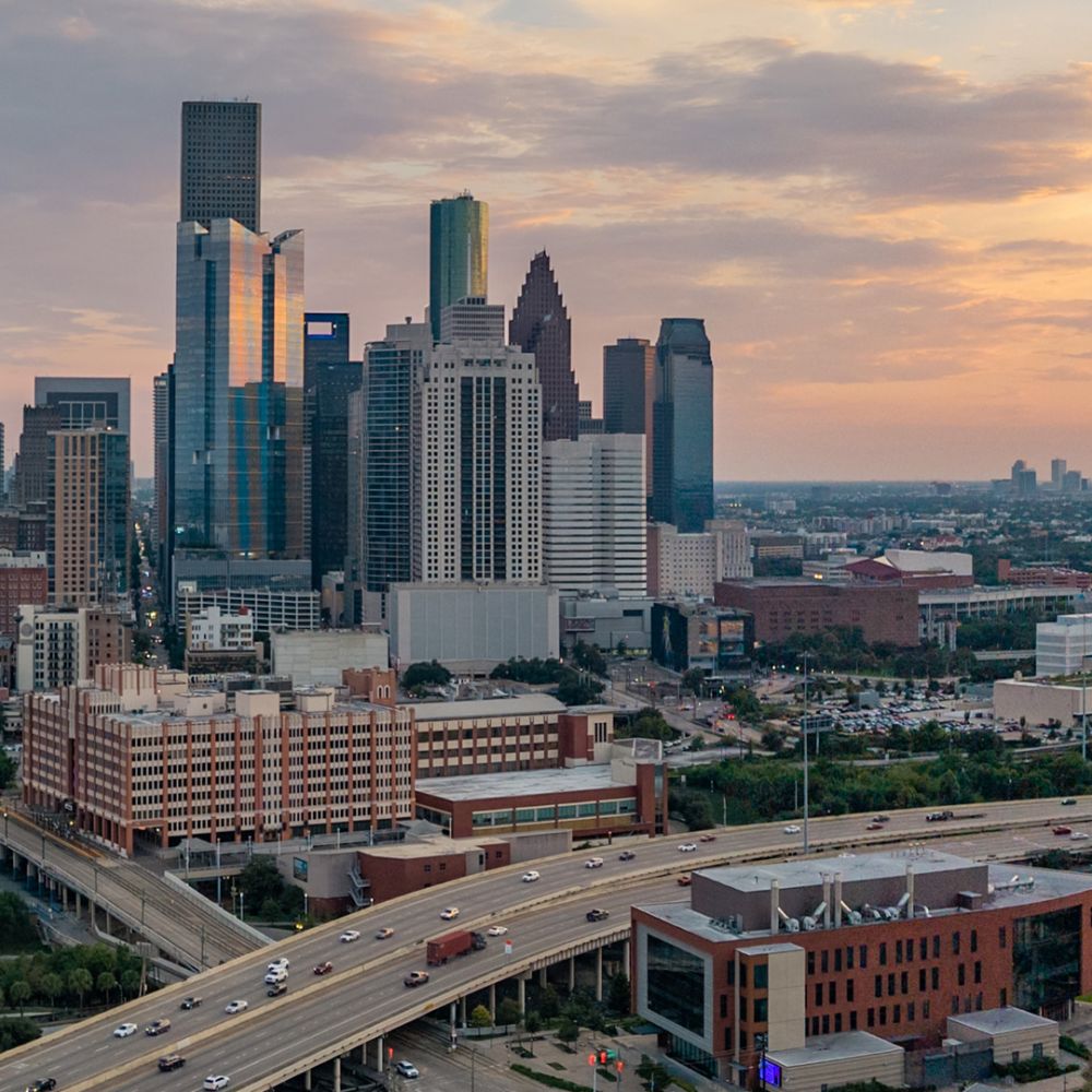 Houston skyline at sunset with modern skyscrapers and highways, showcasing urban architecture and warm sky tones.