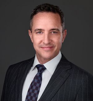 Attorney Matt Horak in a suit smiling against a gray background for a profile or business headshot photo.