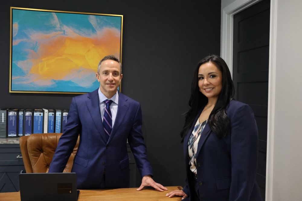 Matthew P. Horak and Nicole Maldonado in suits posing in a modern office with colorful art and file organizers.