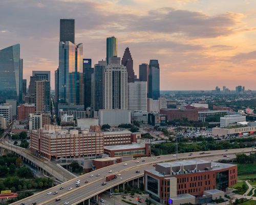 Houston skyline at sunset with modern skyscrapers and highways, showcasing urban architecture and warm sky tones.