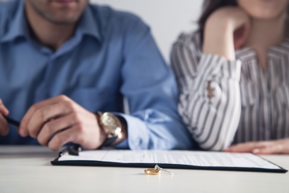 Couple signing divorce papers, with rings on table; concept of separation or legal agreement.