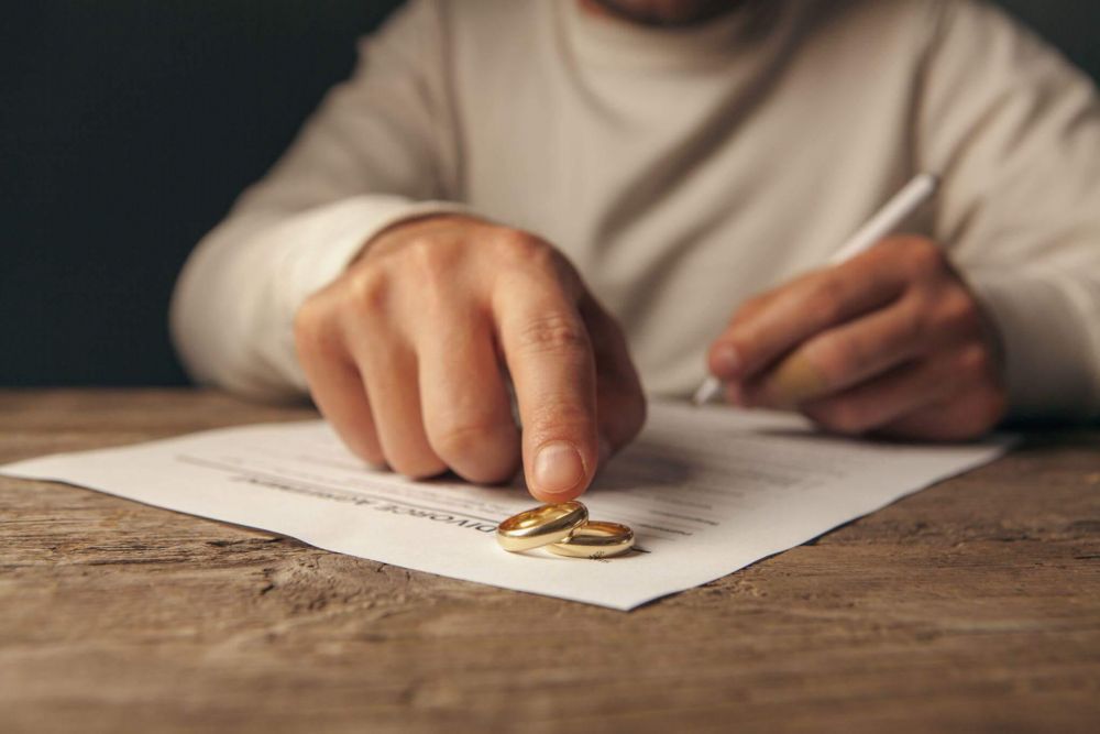 Man signing divorce papers related to a marriage ring.