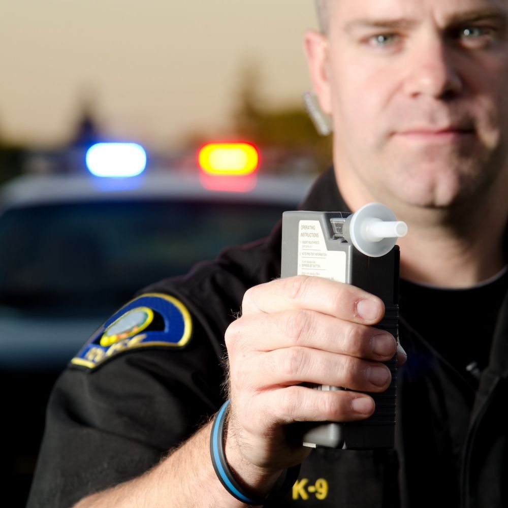 Police officer holding a breathalyzer in front of patrol car with flashing lights, enforcing DUI laws.