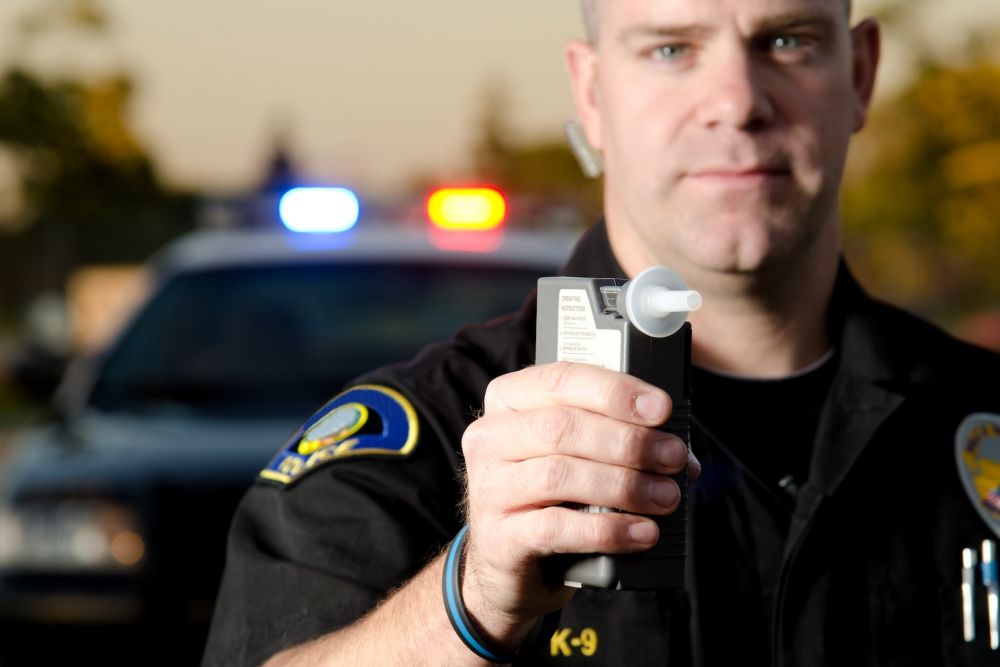 Police officer holding a breathalyzer in front of patrol car with flashing lights, enforcing DUI laws.