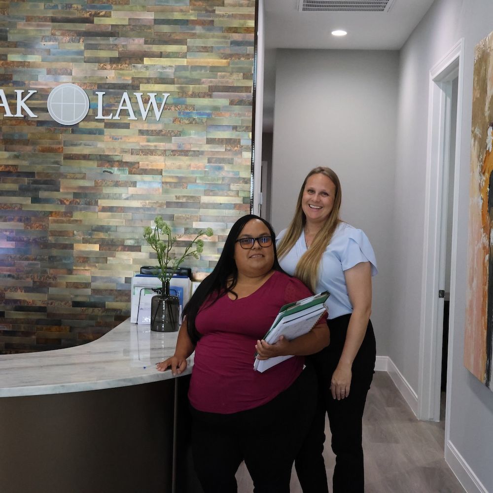 Two women at Horak Law reception desk, modern office setting with artwork and welcoming atmosphere.