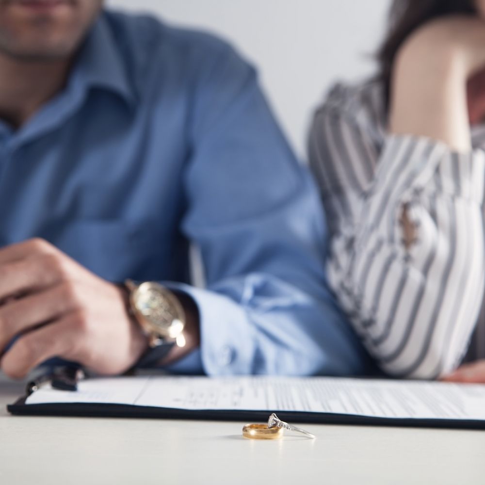 Couple signing divorce papers, with rings on table; concept of separation or legal agreement.