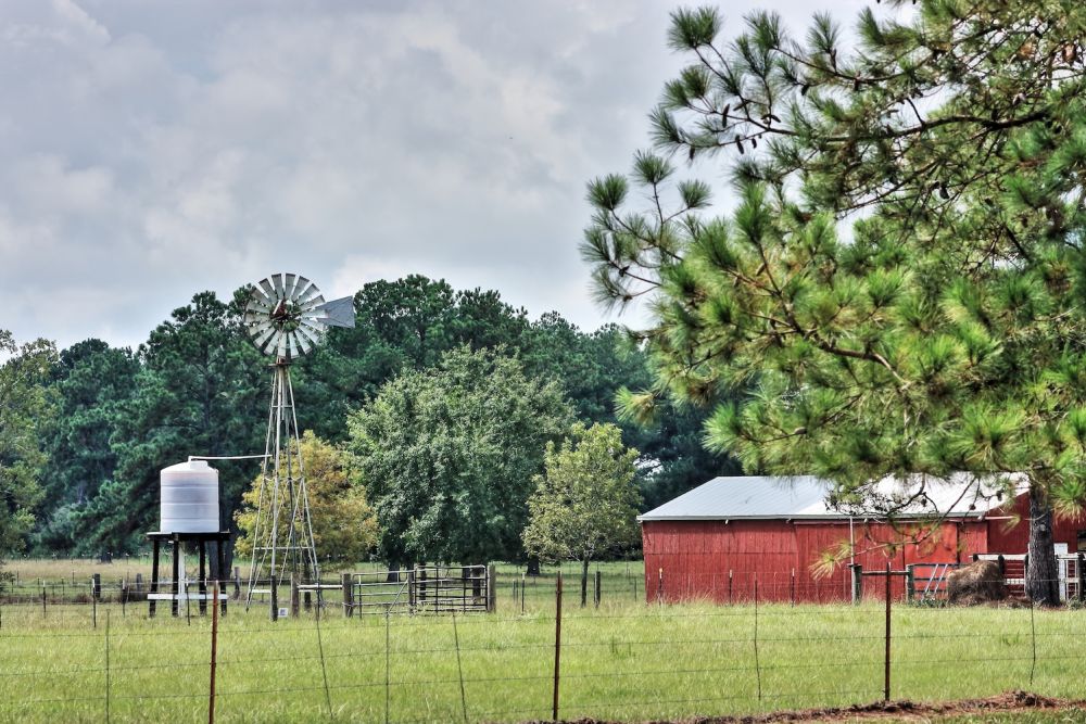 Scenic rural landscape with a windmill, red barn, trees, and spacious green field.
