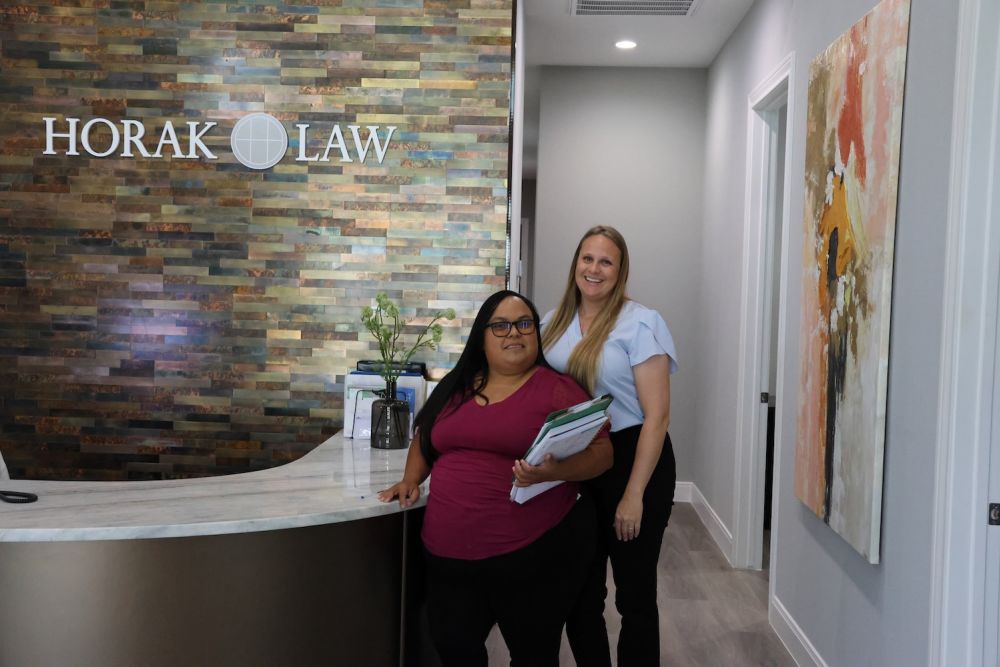 Two women at Horak Law reception desk, modern office setting with artwork and welcoming atmosphere.