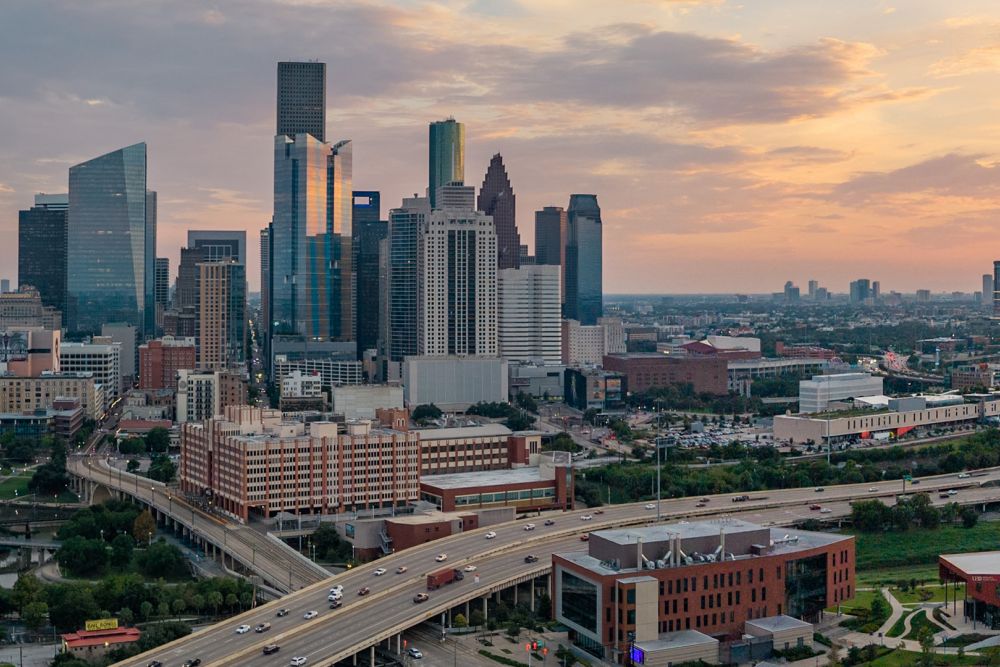 Houston skyline at sunset with modern skyscrapers and highways, showcasing urban architecture and warm sky tones.