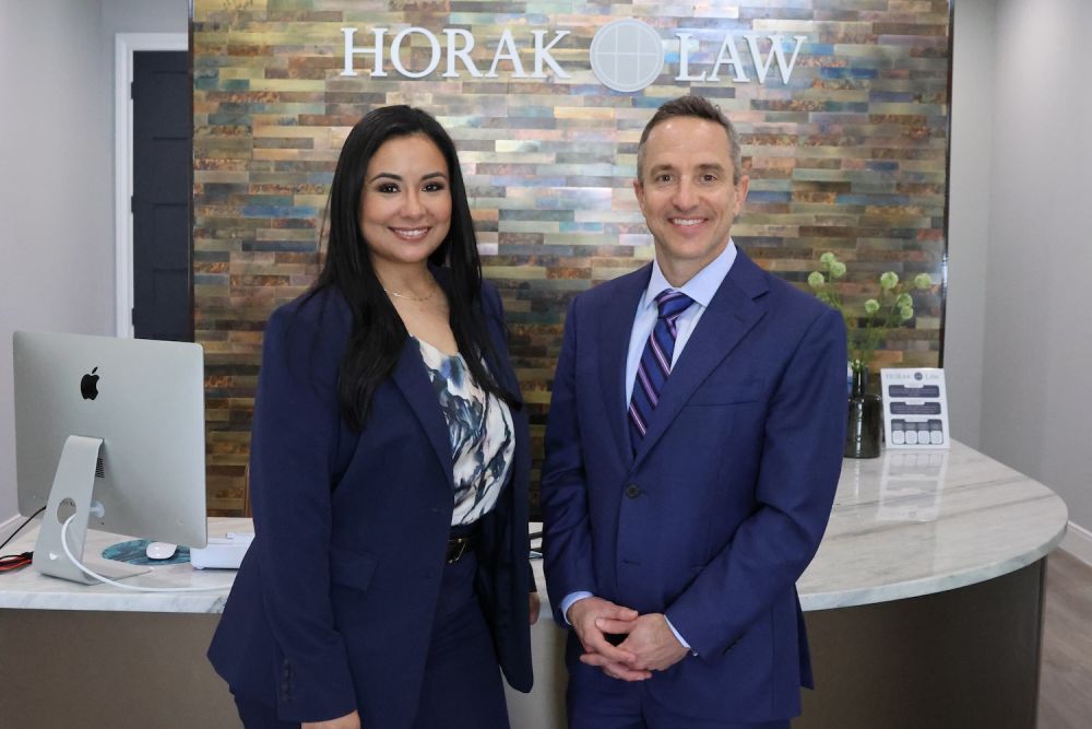 Matthew P. Horak and Nicole Maldonado in navy suits at Horak Law's reception area with a sleek, modern design background.