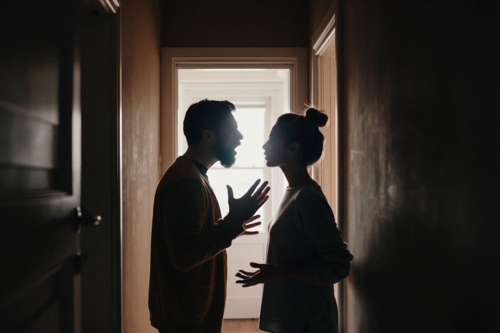 Silhouette of a couple arguing in a dimly lit hallway, illustrating conflict and communication issues.