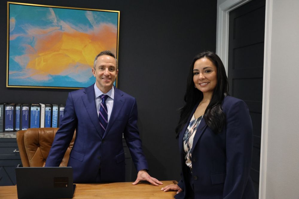 Matthew P. Horak and Nicole Maldonado in a modern office, smiling and standing near a desk with a colorful painting in the background.