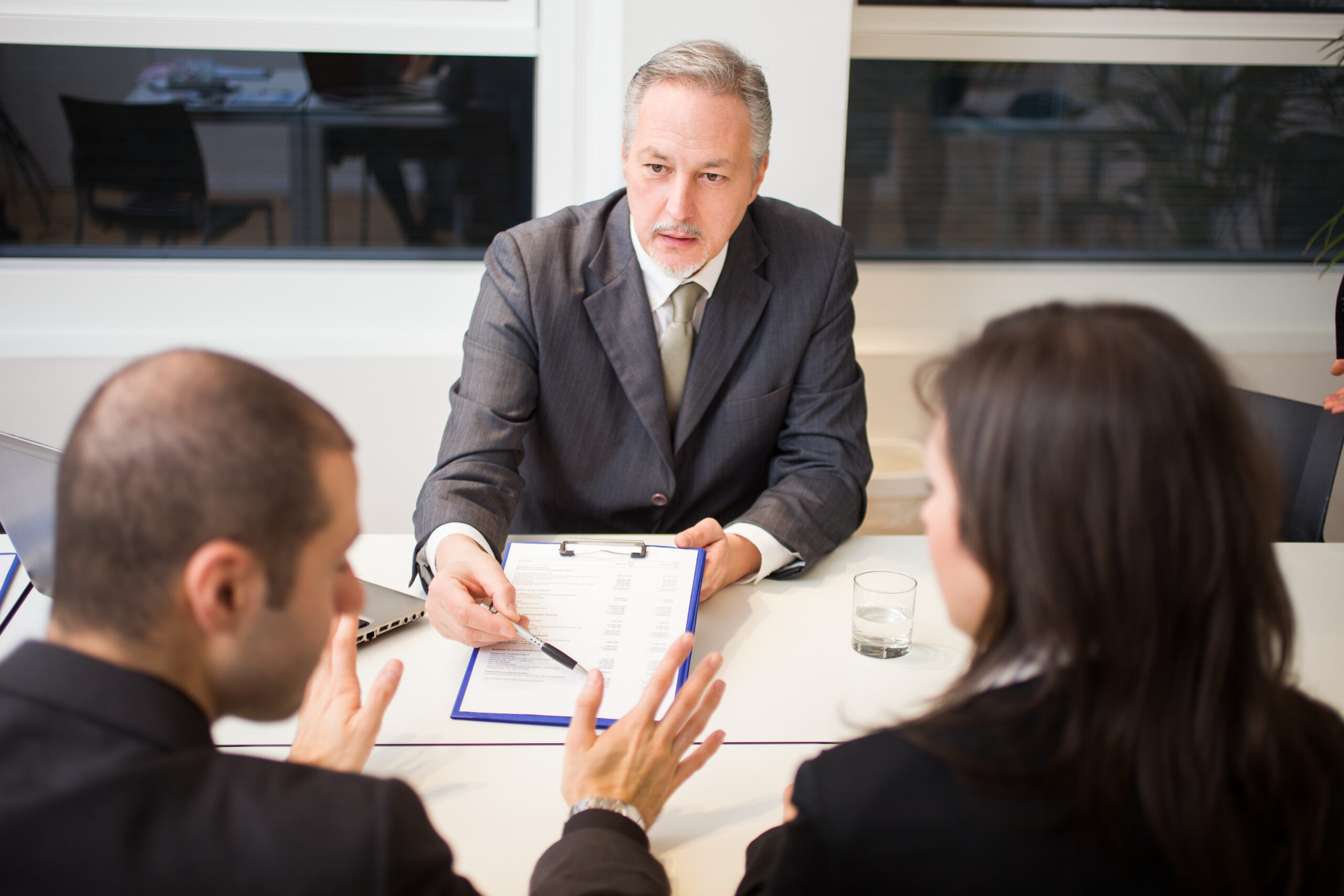 A lawyer in a suit discusses alimony with two clients at a table during a high asset divorce consultation.